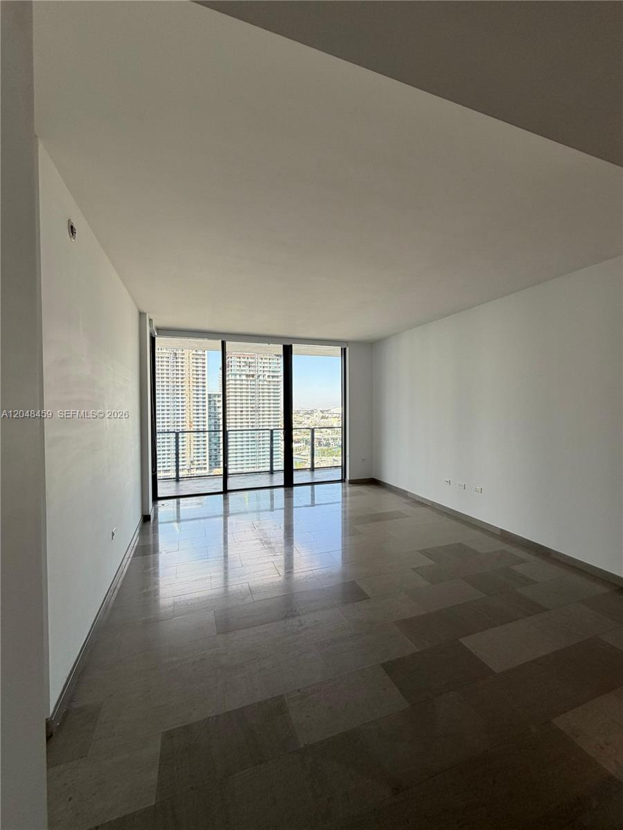 An empty room with large floor-to-ceiling windows, tile flooring, and a balcony view — 68 SE 6th St # 2506, Miami FL 33131, MIAMI, FL