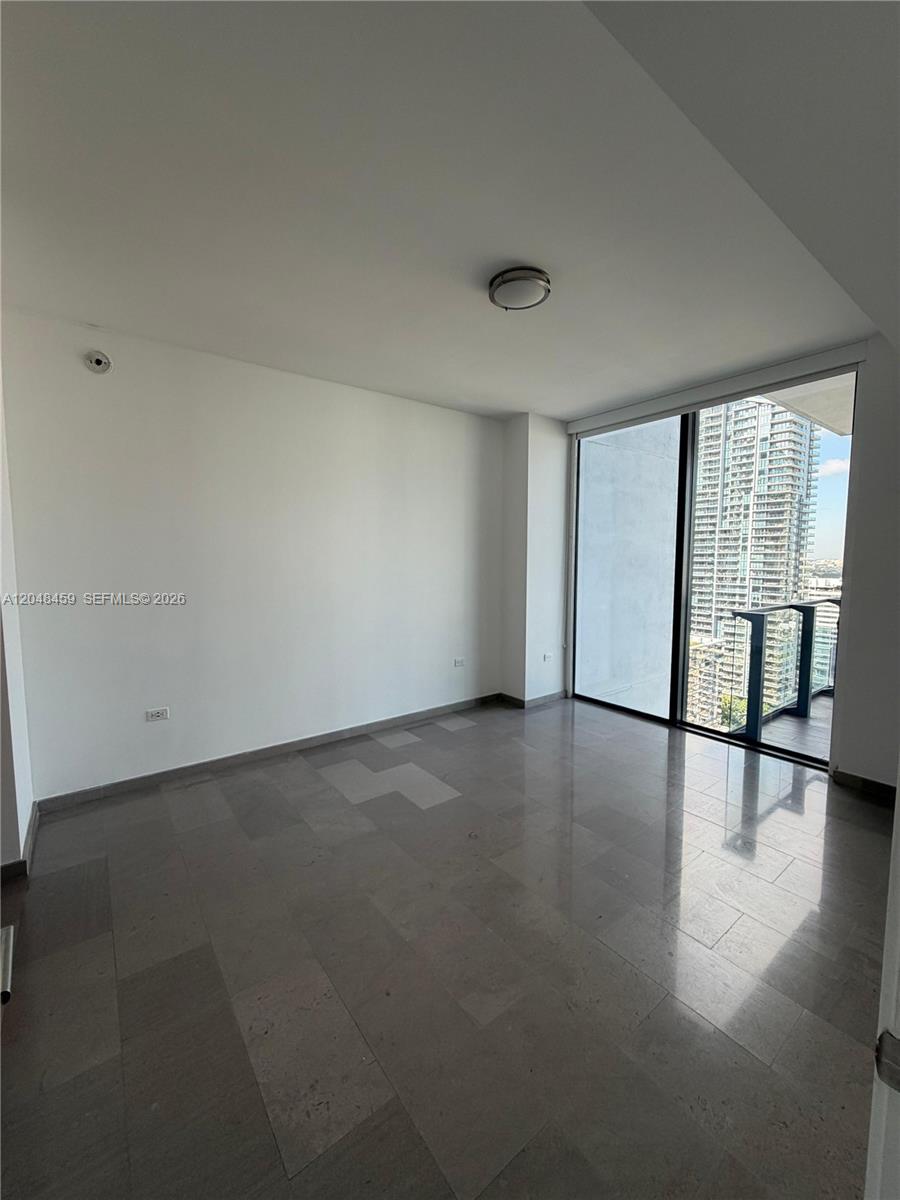 An empty room features gray tile flooring, white walls, and a balcony with city views — 68 SE 6th St # 2506, Miami FL 33131, MIAMI, FL