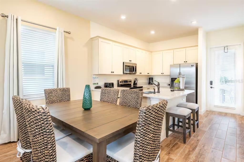 A dining area with a wooden table and wicker chairs sits adjacent to a kitchen — 2998 SALTED RIM ROAD, KISSIMMEE, FL