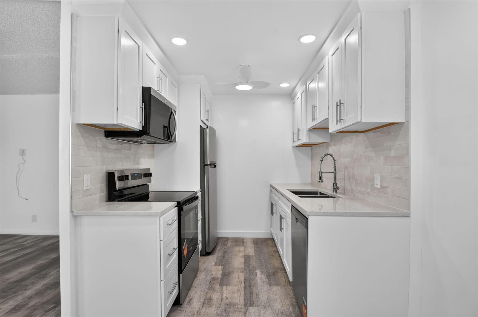 A galley kitchen features white cabinets, stainless steel appliances, light countertops, and wood-look flooring — 3045 Cornwall C, Boca Raton FL 33434, BOCA RATON, FL