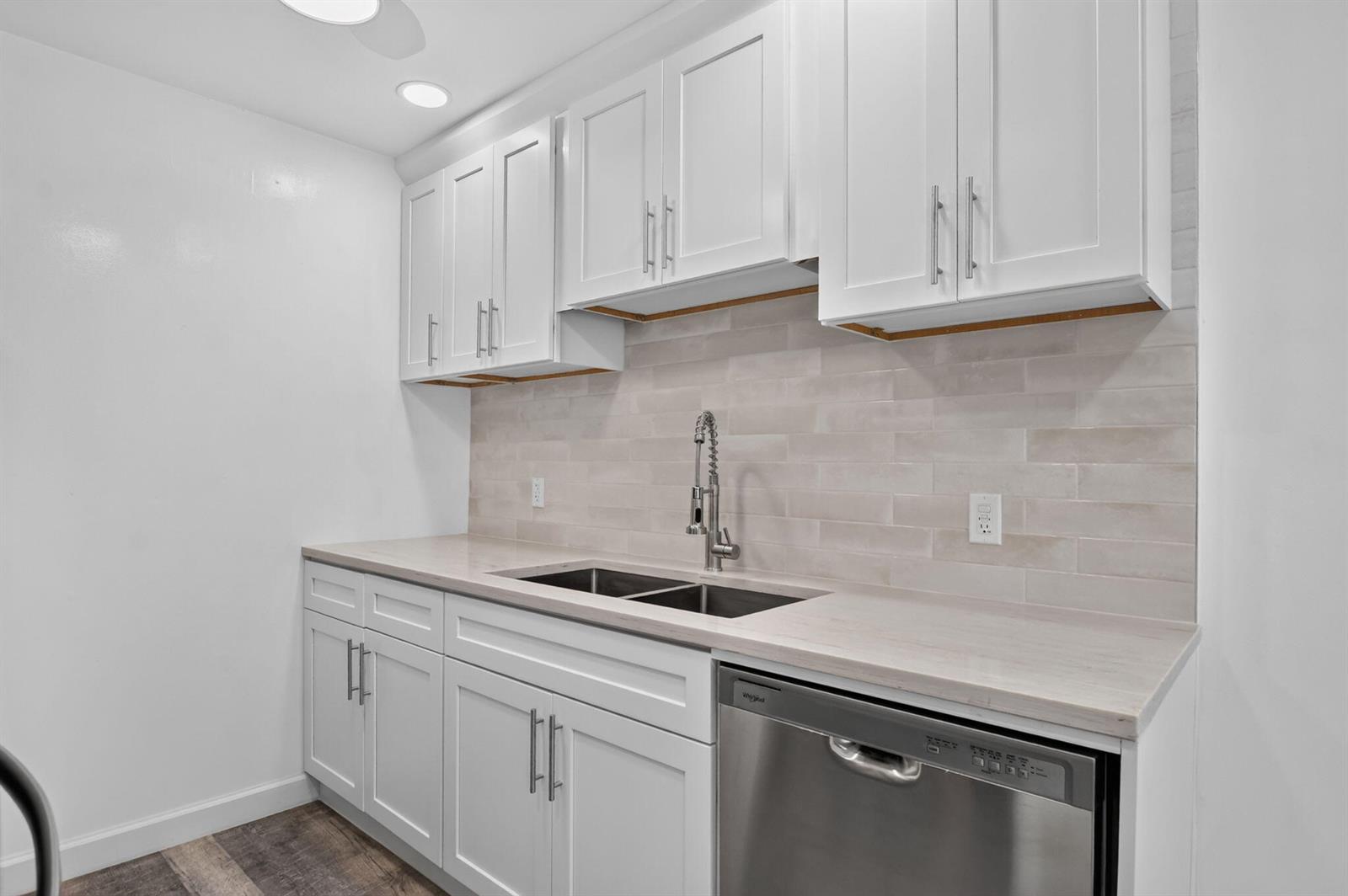 A kitchen featuring white cabinets, a light-colored countertop, a stainless steel dishwasher, and tile backsplash — 3045 Cornwall C, Boca Raton FL 33434, BOCA RATON, FL