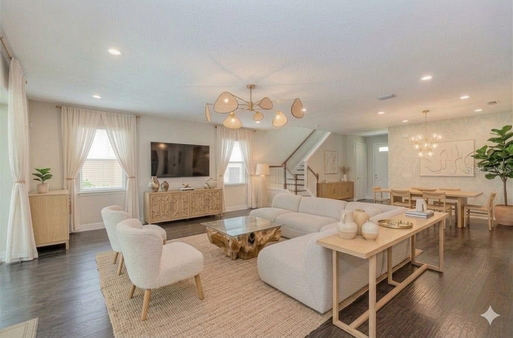 A bright, open-concept living and dining area features modern furniture, a wood-base coffee table, and chandeliers — 1130 POWERSONG STREET, HOLIDAY, FL