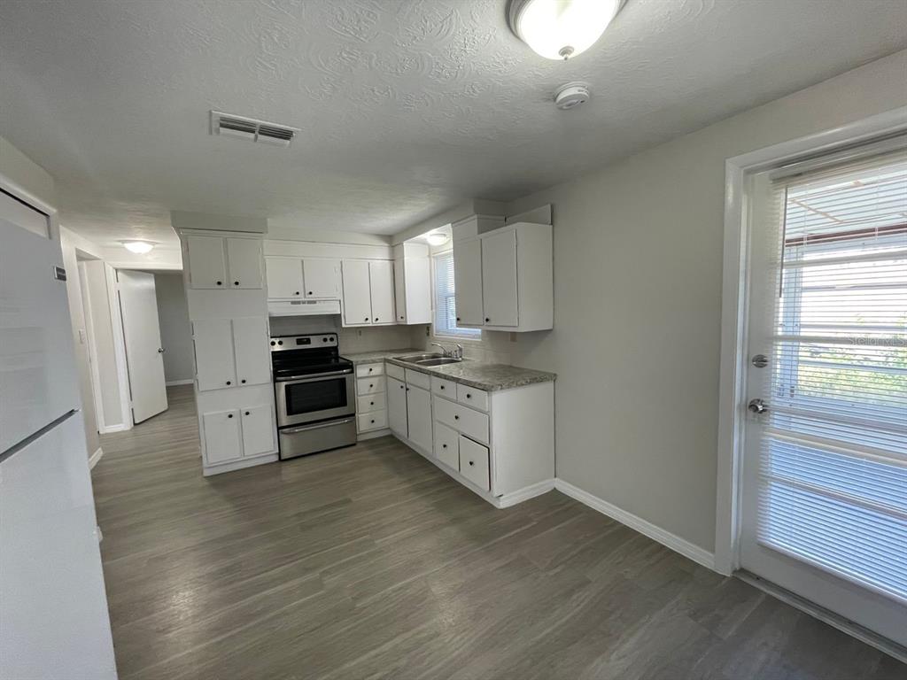 A kitchen features white cabinets, stainless steel appliances, granite countertops, and light wood-look flooring — 1130 POWERSONG STREET, HOLIDAY, FL