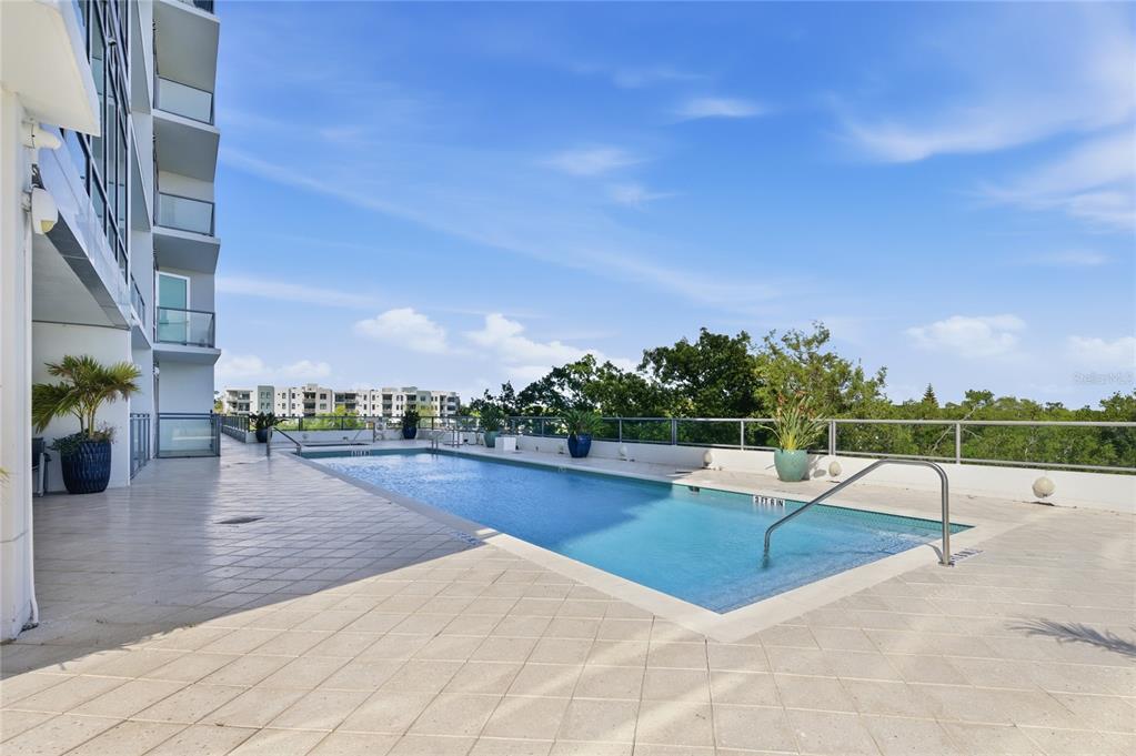An elevated outdoor swimming pool with a tiled deck sits beside a modern apartment building — 101 S EOLA DRIVE UNIT 519, ORLANDO, FL