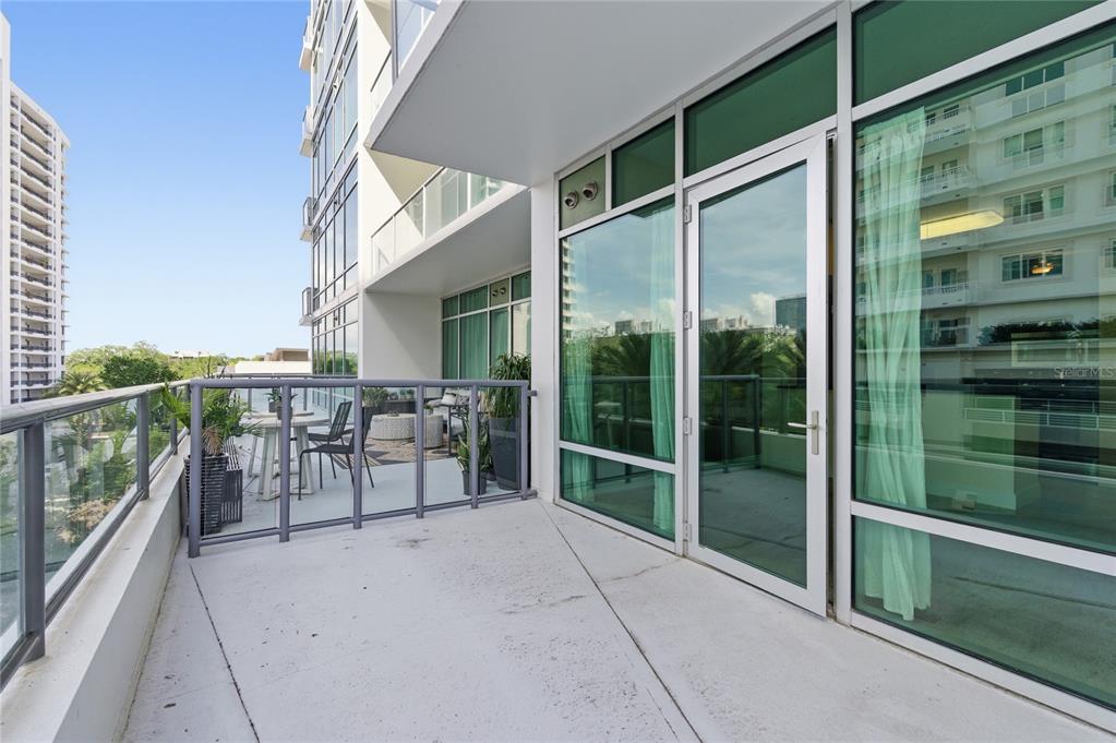 A modern apartment balcony features a glass railing, outdoor seating, and floor-to-ceiling windows — 101 S EOLA DRIVE UNIT 519, ORLANDO, FL