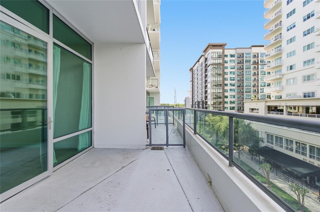 A concrete balcony with a glass railing overlooks a city street and neighboring apartment buildings — 101 S EOLA DRIVE UNIT 519, ORLANDO, FL