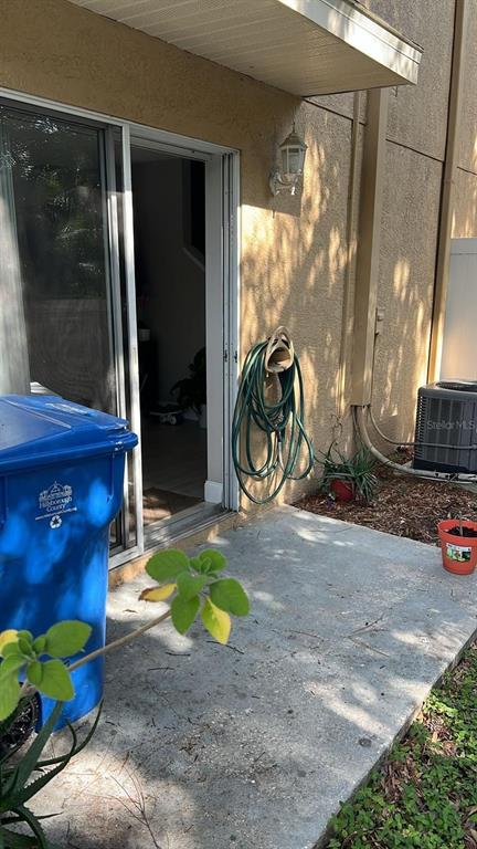 A concrete patio features a sliding glass door, a wall-mounted garden hose, and a trash bin — 8423 EDGEWATER PLACE BOULEVARD, TAMPA, FL