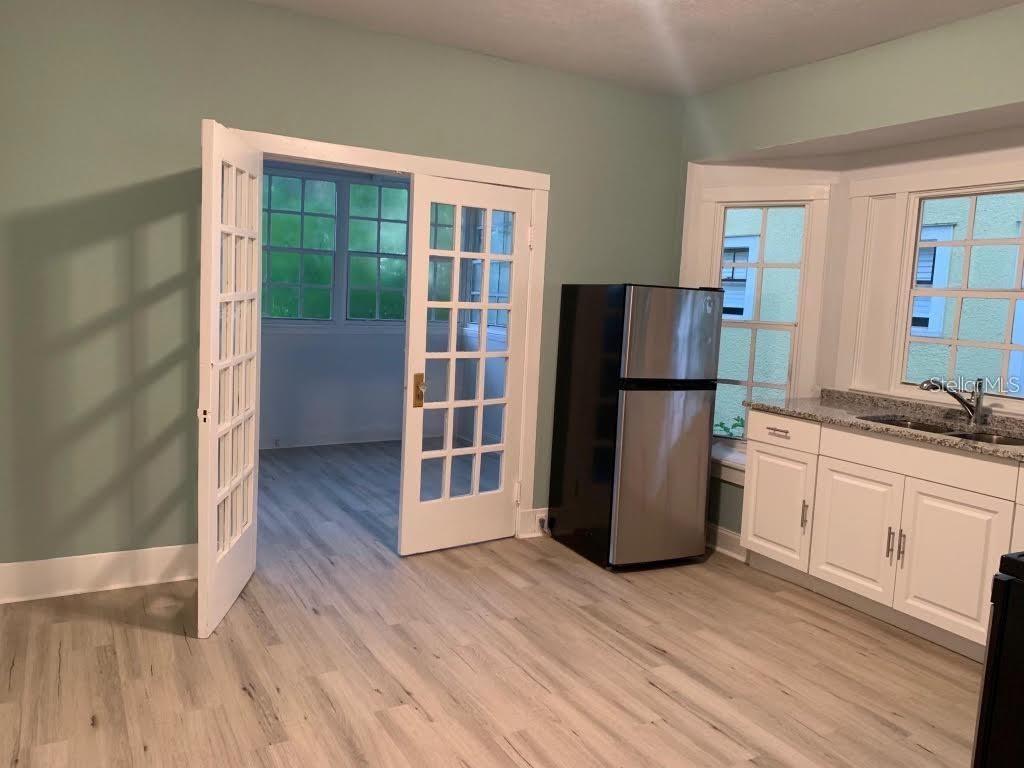 A kitchen with white cabinets and a stainless steel refrigerator opens into a sunroom — 510 N SUMMERLIN AVENUE, ORLANDO, FL
