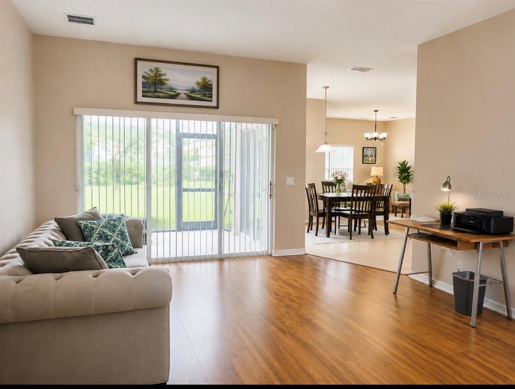 A living room with wood-look flooring, a beige sofa, and a desk leads to a dining area — 3578 VALLEYVIEW DRIVE, KISSIMMEE, FL