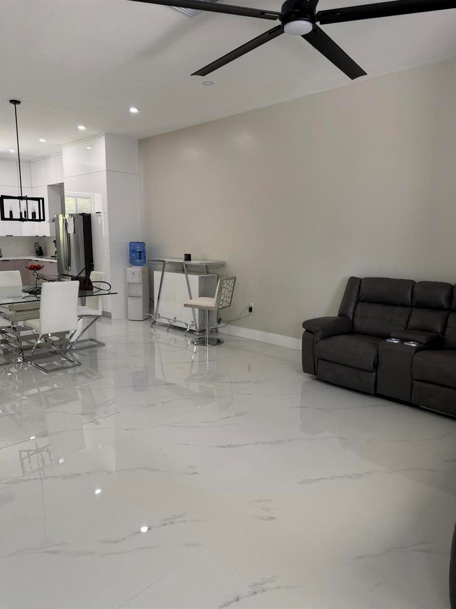 A living room with white marble-look tile flooring, a dark leather sofa, and a ceiling fan — 1101 Yeehaw Avenue, Clewiston FL 33440, CLEWISTON, FL