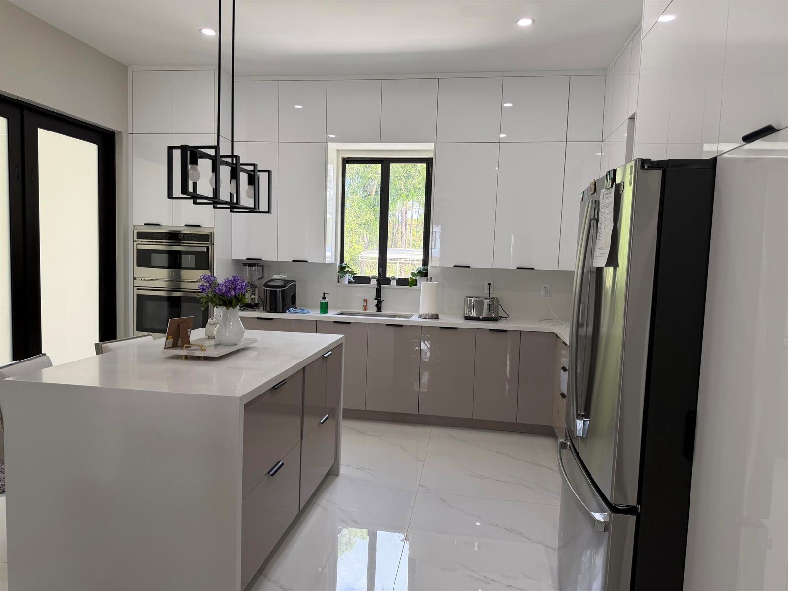 A modern kitchen features white upper cabinets, taupe lower cabinets, a white island, and stainless appliances — 1101 Yeehaw Avenue, Clewiston FL 33440, CLEWISTON, FL