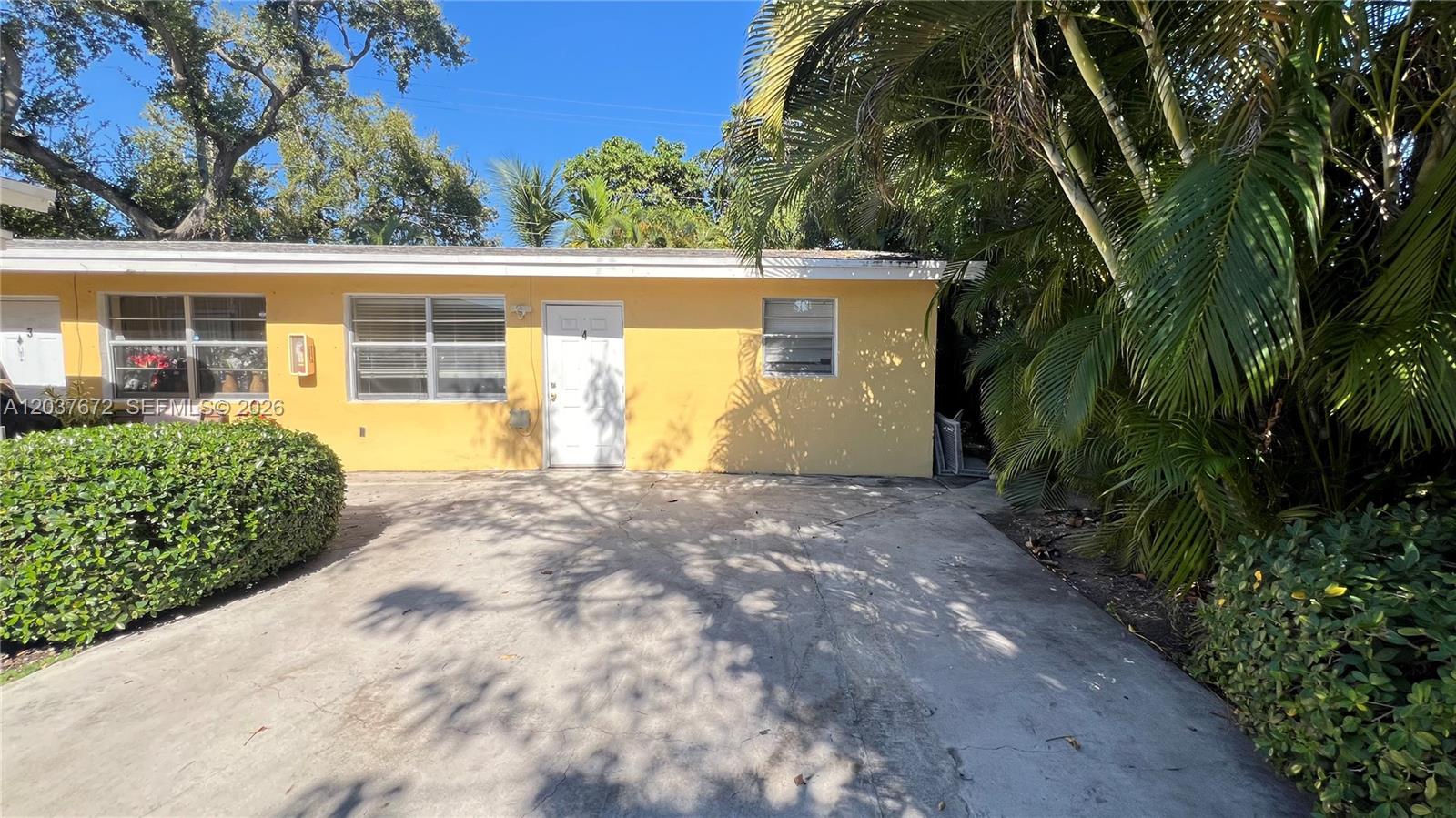 A yellow single-story building exterior features a concrete driveway and a white entry door — 706 SW 4th Ter # 4, Dania Beach FL 33004, DANIA BEACH, FL