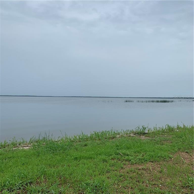 A grassy shoreline overlooks a large, calm body of water under a cloudy sky — 1061 ENTERPRISE OSTEEN ROAD, DELTONA, FL