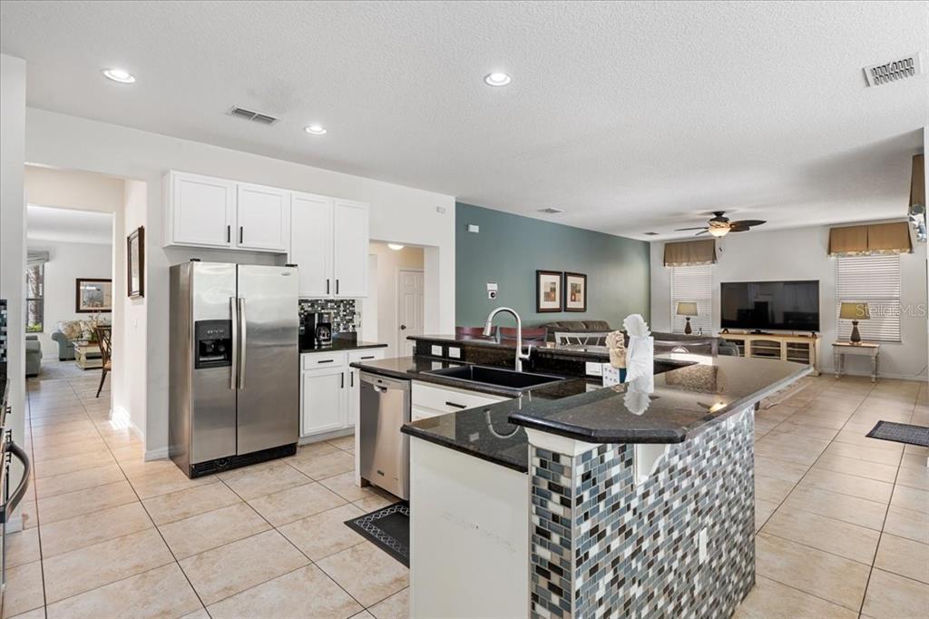 A kitchen with white cabinets, stainless steel appliances, and a tiled island with granite countertops — 211 LAS FUENTES DRIVE, KISSIMMEE, FL