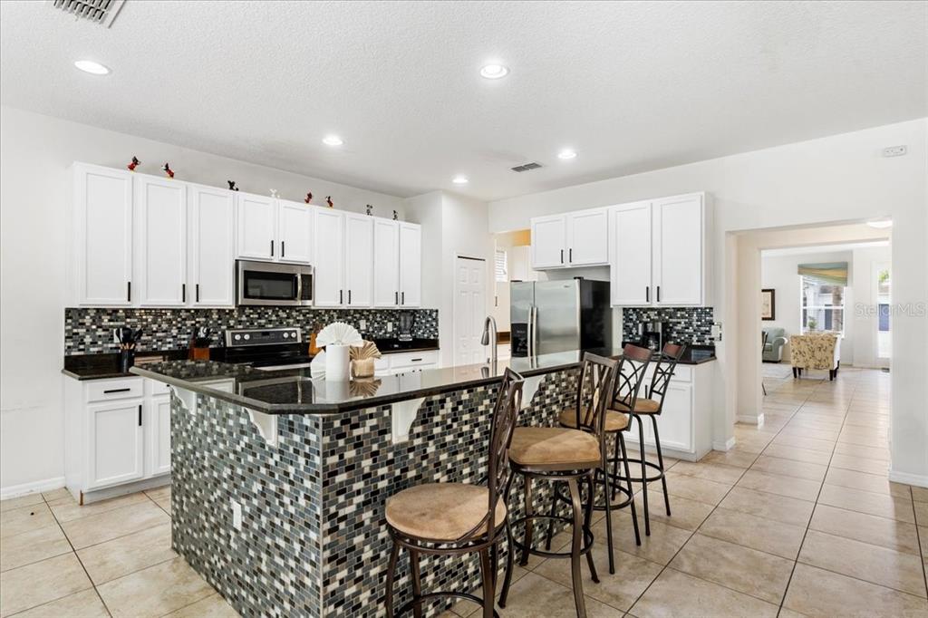 A kitchen features white cabinets, dark granite countertops, and a tiled island with bar stools — 211 LAS FUENTES DRIVE, KISSIMMEE, FL