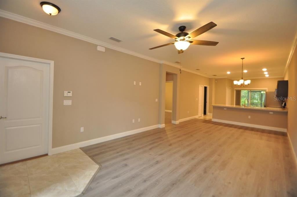 An open-concept living area with light wood-look flooring, beige walls, and a kitchen in back — 11 ULLYNN PLACE UNIT B, PALM COAST, FL