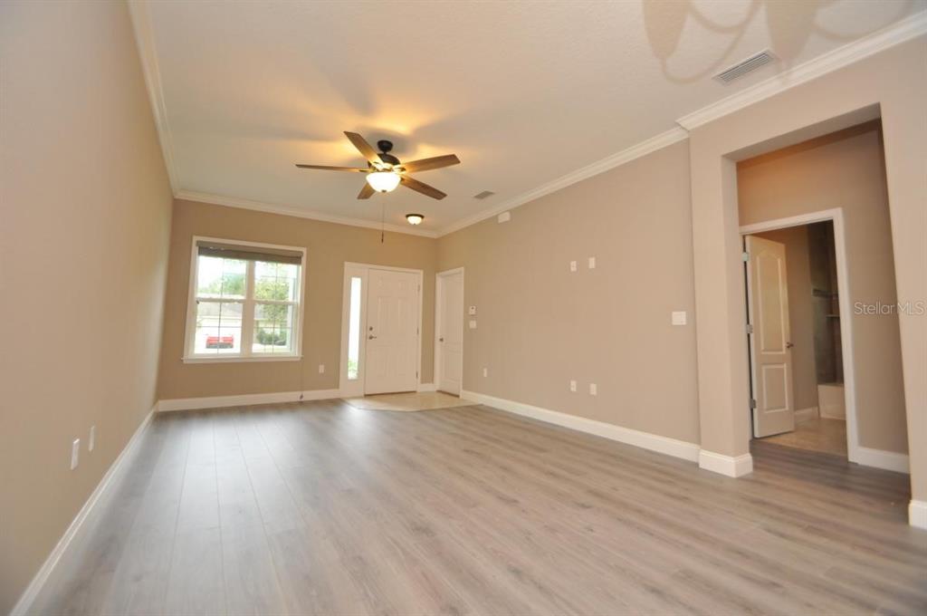 A living room with light-colored walls, wood-look flooring, a ceiling fan, and an entryway door — 11 ULLYNN PLACE UNIT B, PALM COAST, FL