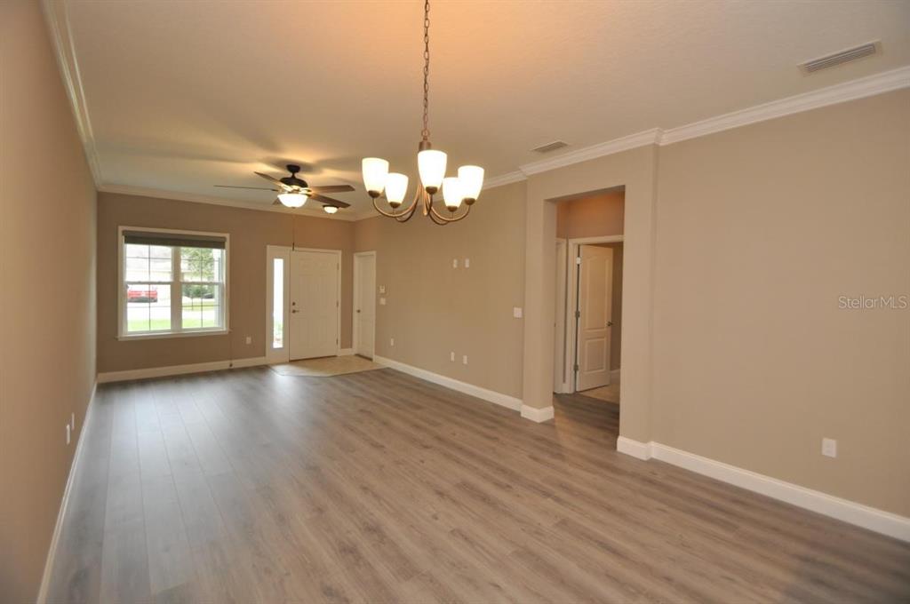 An empty living room features light wood-look flooring, a chandelier, and a ceiling fan — 11 ULLYNN PLACE UNIT B, PALM COAST, FL