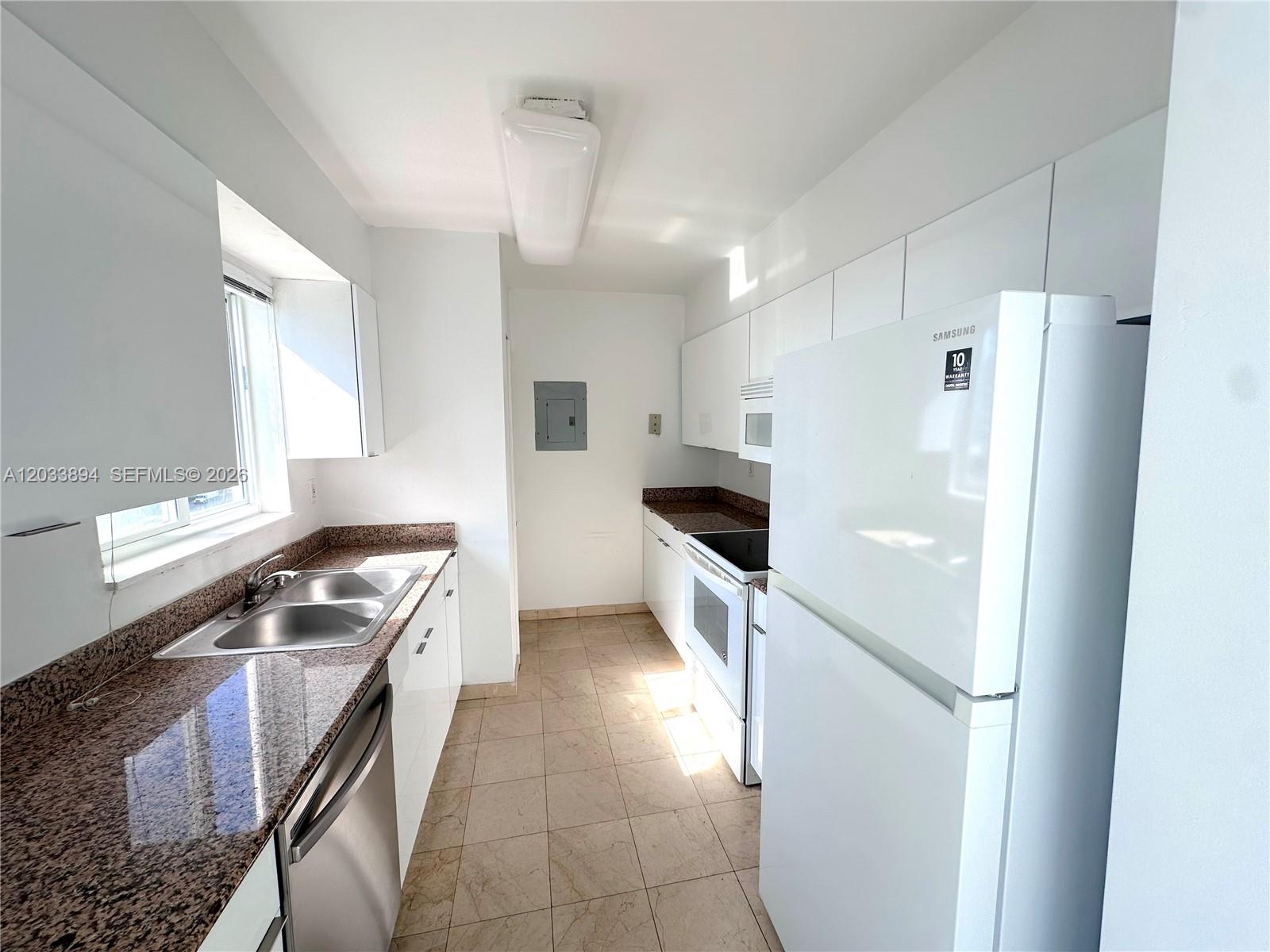 A galley kitchen features white cabinets, granite countertops, stainless steel appliances, and tile flooring — 5900 Collins Ave # 906, Miami Beach FL 33140, MIAMI BEACH, FL