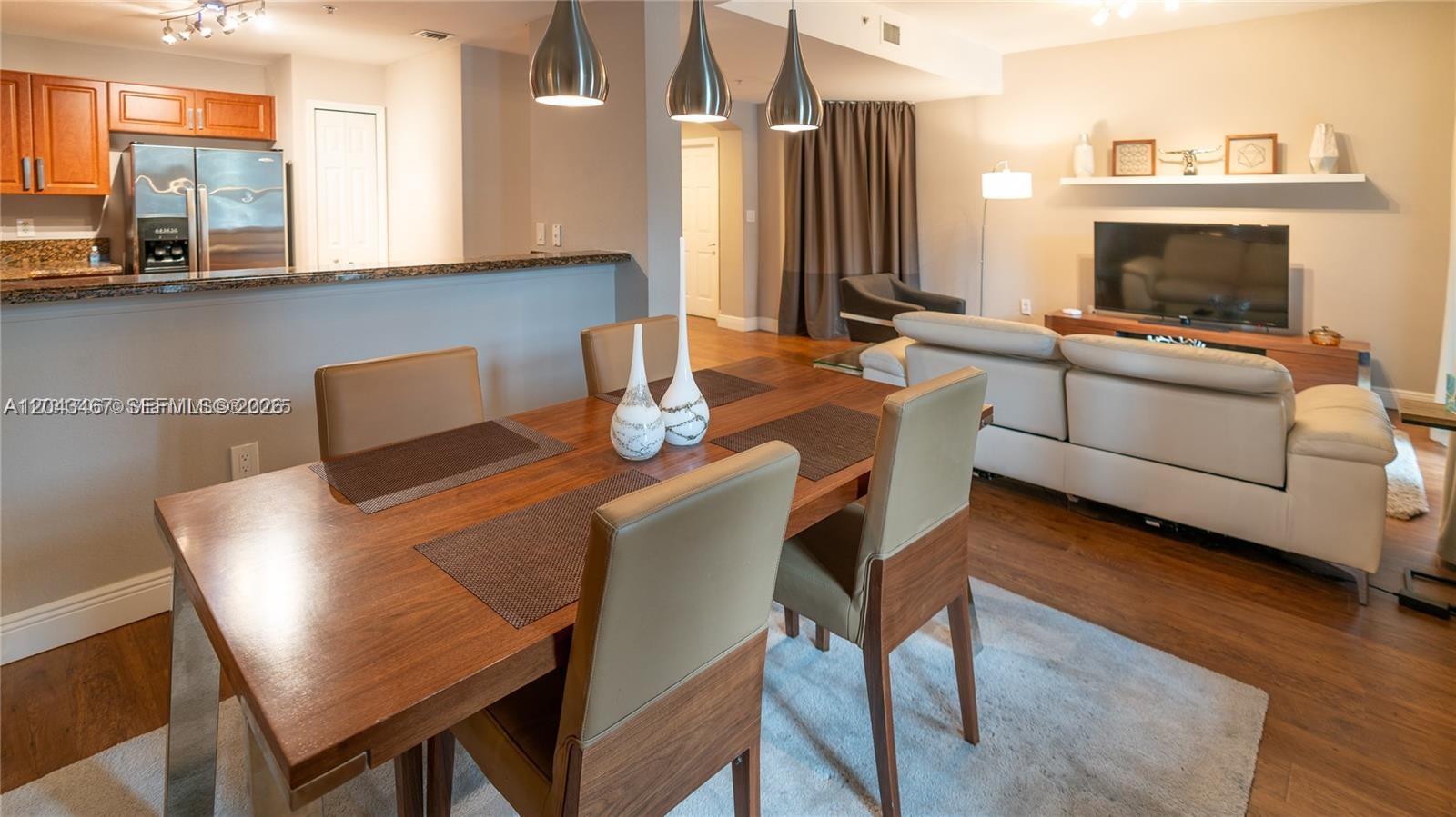 An open-concept dining and living area features wood flooring, a wooden table, and modern lighting — 11002 NW 83rd St # 106, Doral FL 33178, DORAL, FL