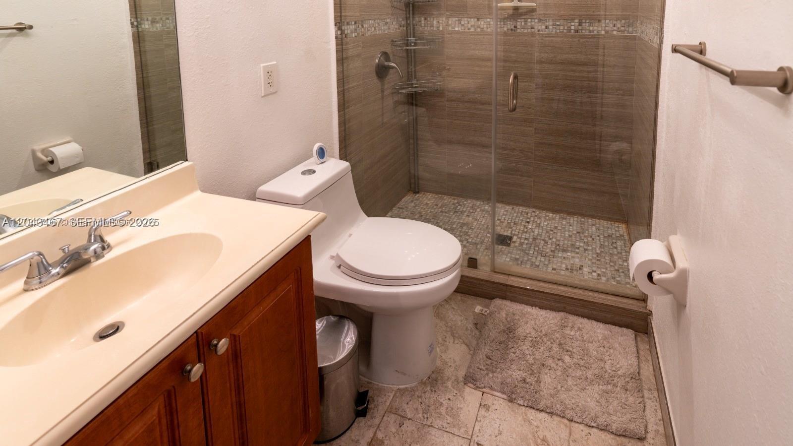 A bathroom features a wooden vanity, a white toilet, and a glass-enclosed tiled shower — 11002 NW 83rd St # 106, Doral FL 33178, DORAL, FL