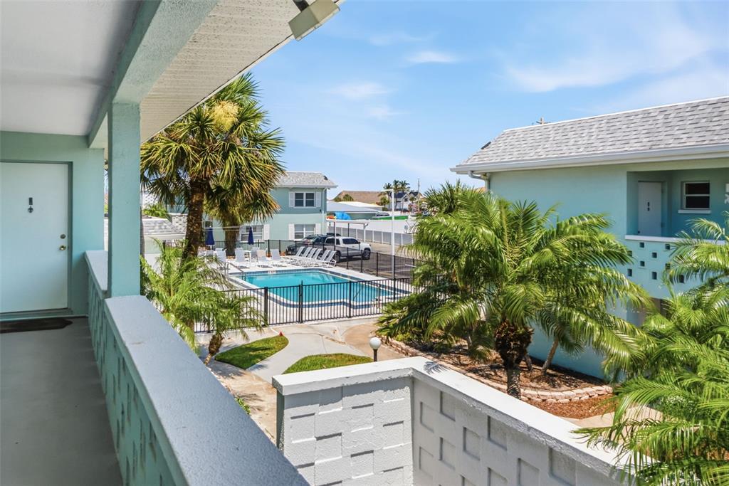 An elevated view from a balcony overlooks a swimming pool and palm trees — 611 GULF DRIVE N UNIT C27, BRADENTON BEACH, FL