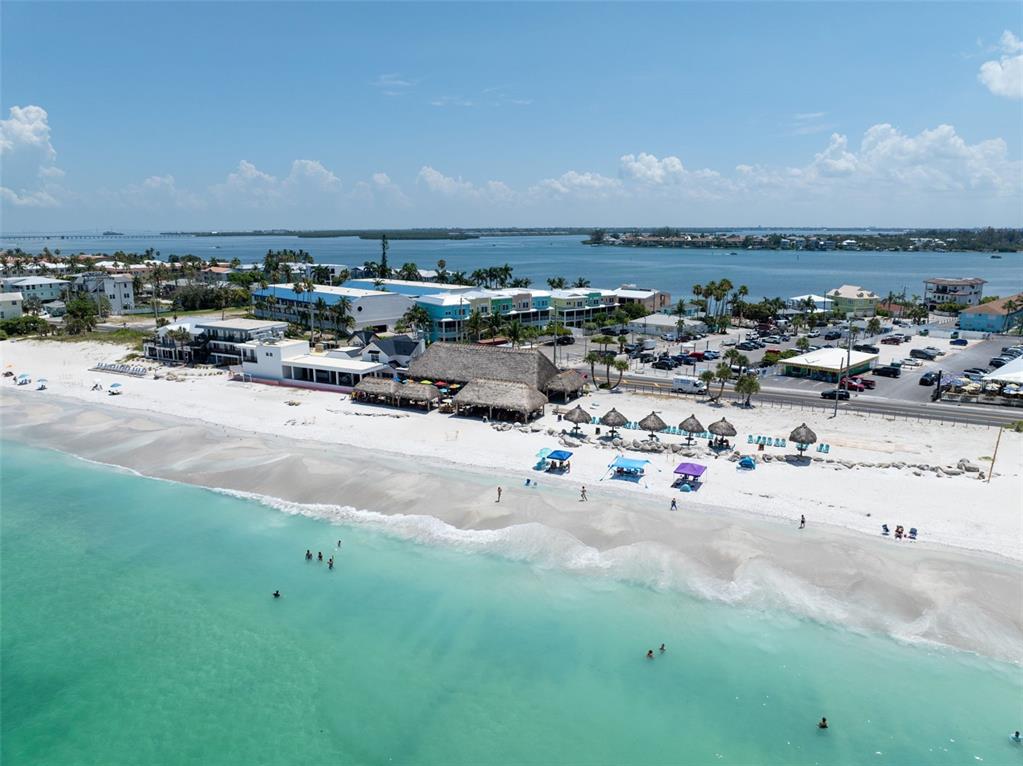 An aerial view shows a sandy beach with thatched-roof structures, umbrellas, and nearby coastal buildings — 611 GULF DRIVE N UNIT C27, BRADENTON BEACH, FL