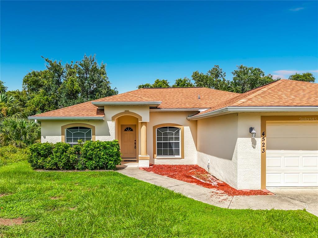 A single-story house with a tan stucco exterior, a brown shingled roof, and a garage — 4523 BUTTERFLY LANE, NORTH PORT, FL