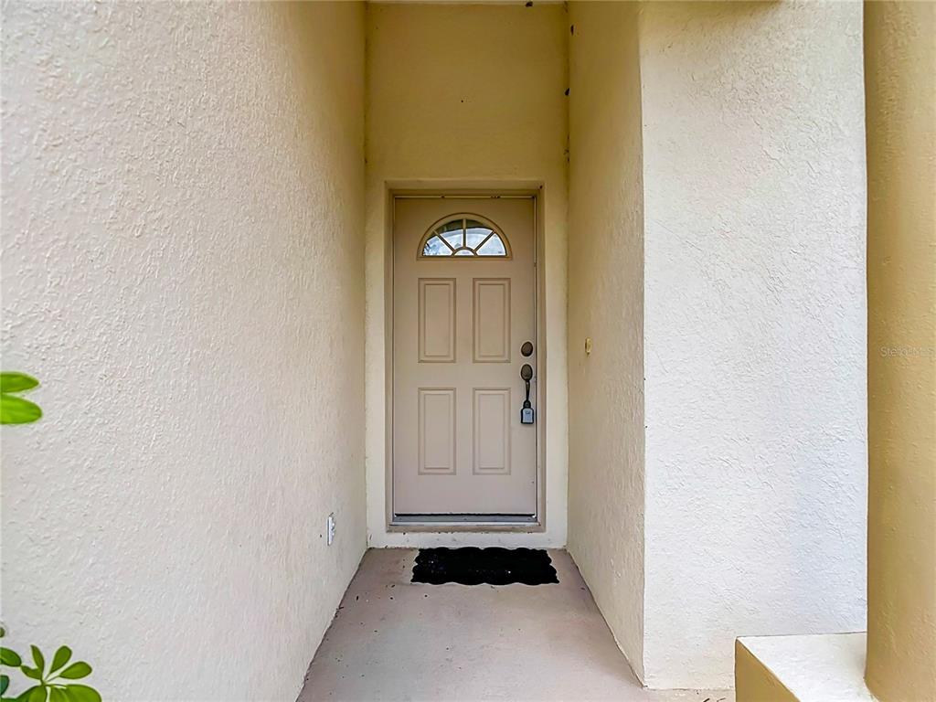 A beige front door with a small arched window sits at the end of a porch — 4523 BUTTERFLY LANE, NORTH PORT, FL
