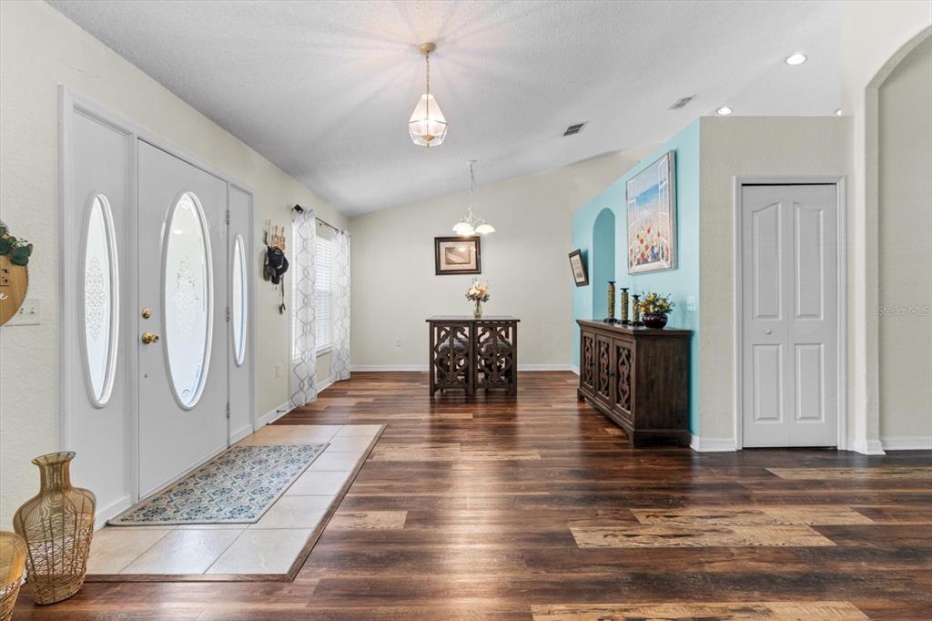 An entryway with wood-look flooring leads to a dining area with a vaulted ceiling — 16038 MALDEN ROAD, WEEKI WACHEE, FL