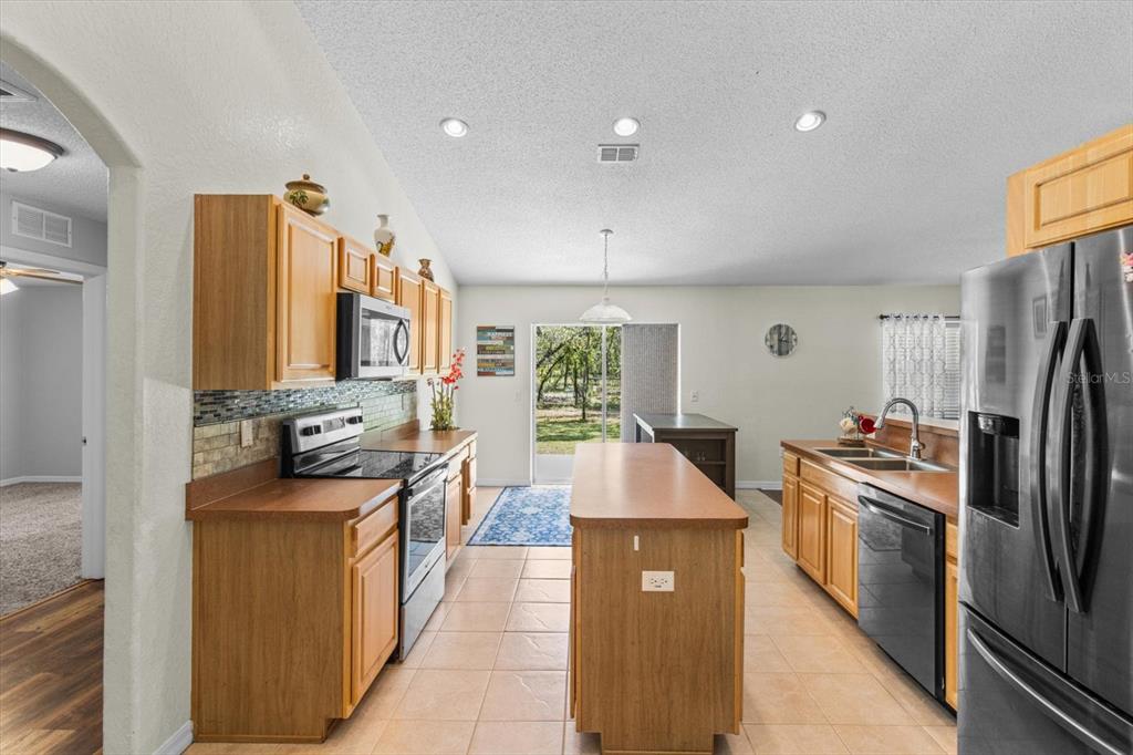 A kitchen features wood cabinets, a central island, stainless steel appliances, and tile flooring — 16038 MALDEN ROAD, WEEKI WACHEE, FL