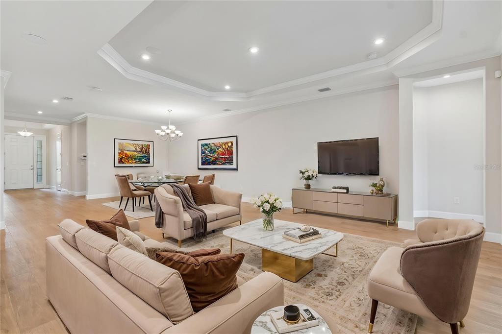A living room with a tray ceiling, light wood floors, and a marble coffee table — 29306 GINNETTO DRIVE, WESLEY CHAPEL, FL