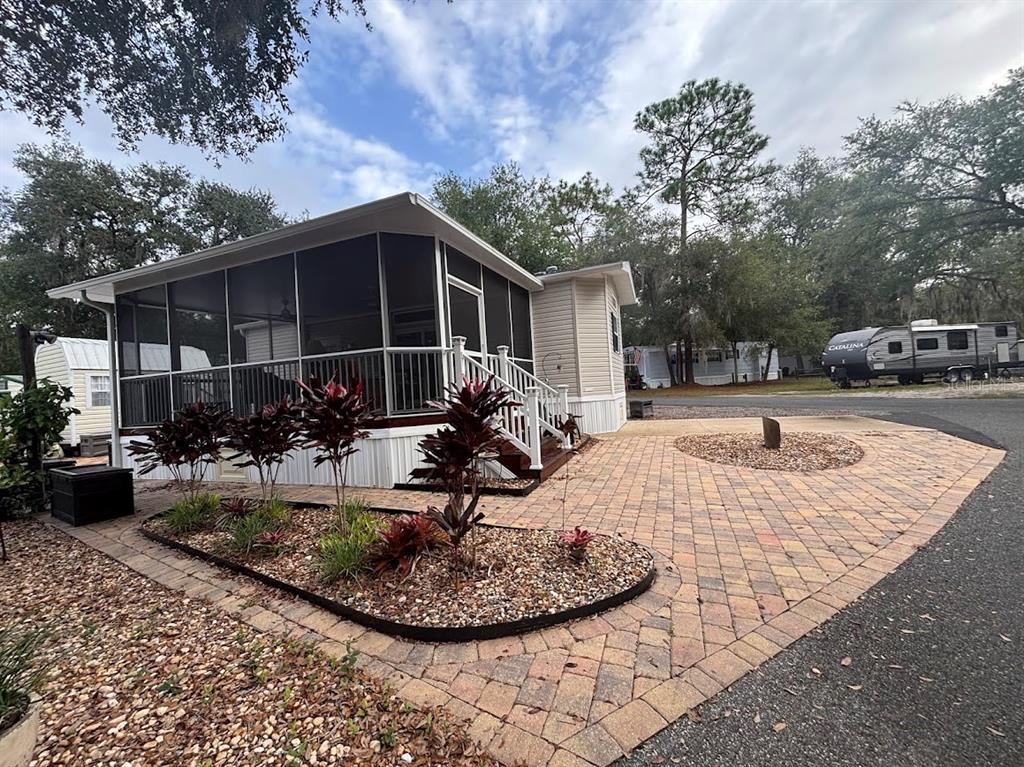 A manufactured home features a large screened-in porch and a paved brick patio area — 25235 NE 143RD PLACE UNIT 145, SALT SPRINGS, FL