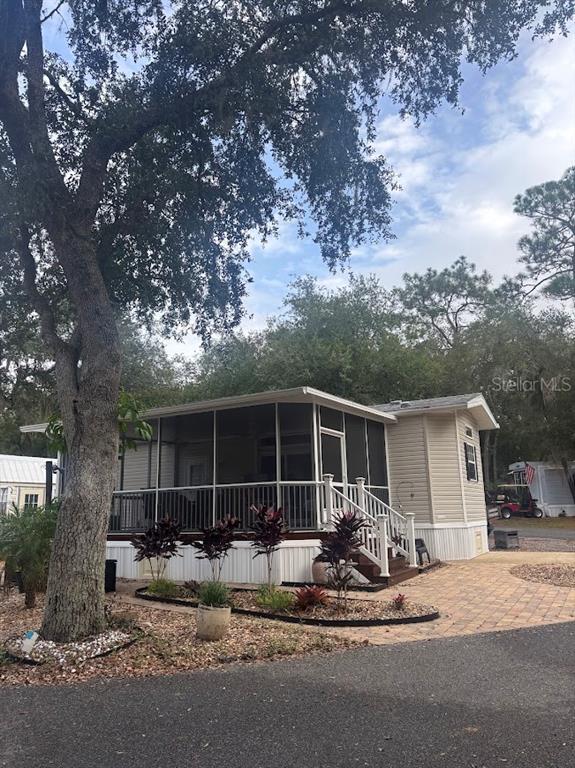 A mobile home with a screened-in porch, light siding, and a paved driveway under trees — 25235 NE 143RD PLACE UNIT 145, SALT SPRINGS, FL