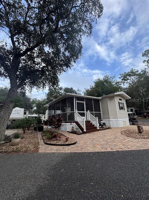 A mobile home with a screened-in porch and paver patio sits under a large tree — 25235 NE 143RD PLACE UNIT 145, SALT SPRINGS, FL