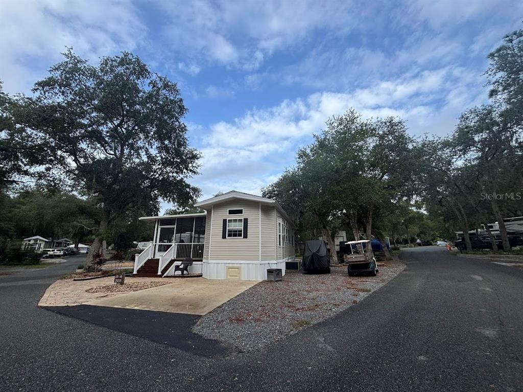 A light-colored manufactured home with a screened porch sits on a corner lot — 25235 NE 143RD PLACE UNIT 145, SALT SPRINGS, FL