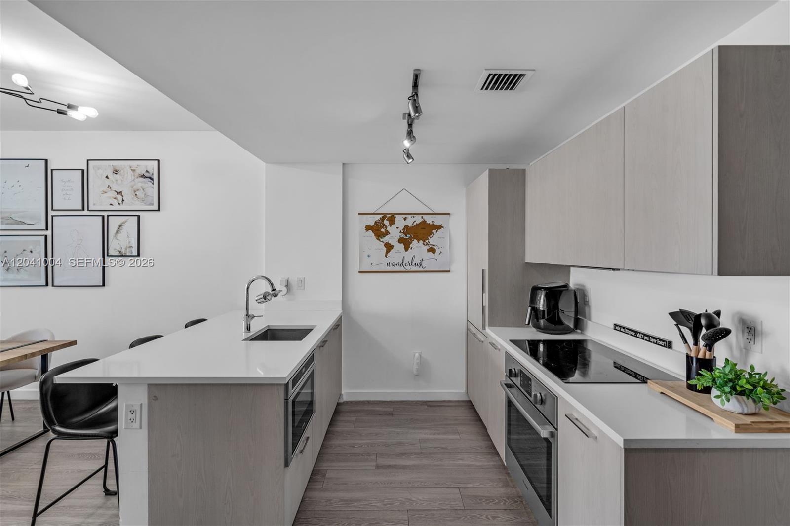 A modern kitchen features light wood cabinetry, white countertops, stainless steel appliances, and a breakfast bar — 501 NE 31st St # 3704, Miami FL 33137, MIAMI, FL