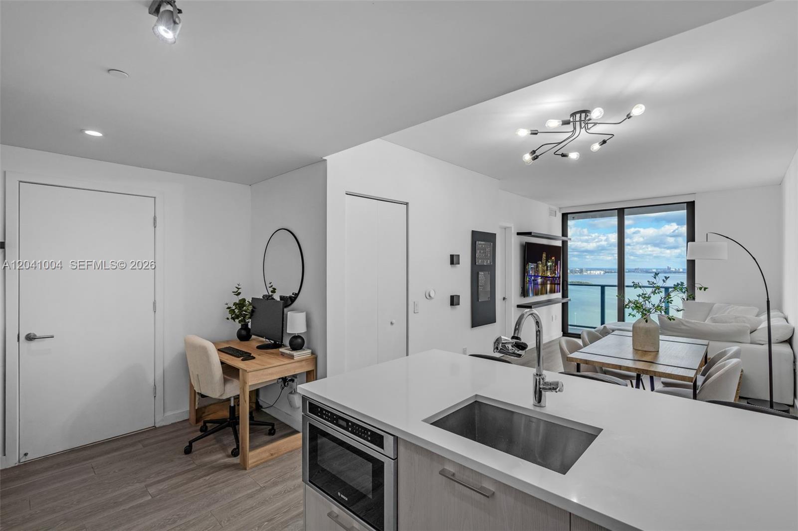 A modern kitchen island overlooks a living area with a dining table and water views — 501 NE 31st St # 3704, Miami FL 33137, MIAMI, FL