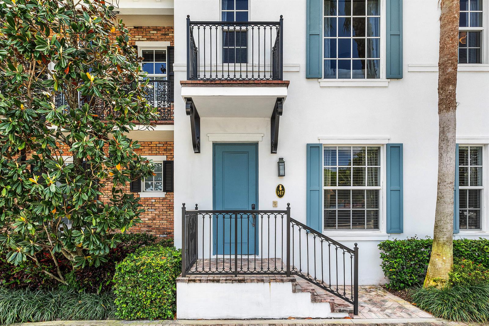 A white townhouse exterior features a blue front door, a small balcony, and metal railings — 147 N Cannery Row Circle, Delray Beach FL 33444, DELRAY BEACH, FL