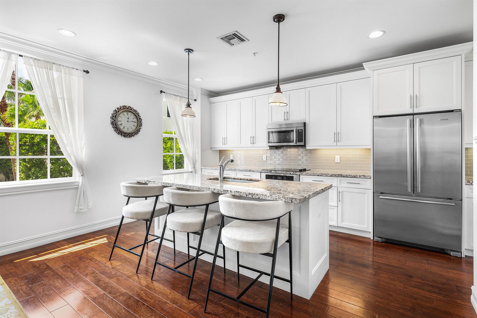 A kitchen features white cabinets, granite countertops, a central island with stools, and hardwood floors — 147 N Cannery Row Circle, Delray Beach FL 33444, DELRAY BEACH, FL
