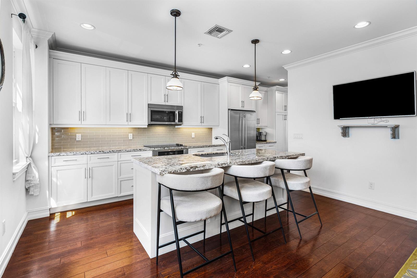 A kitchen features white cabinets, granite countertops, a central island with stools, and hardwood floors — 147 N Cannery Row Circle, Delray Beach FL 33444, DELRAY BEACH, FL