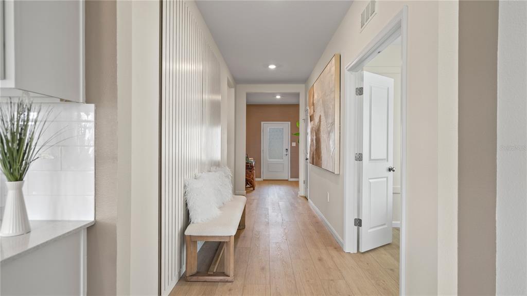 A hallway features light wood flooring, a white bench, and a large abstract wall painting — 3129 ROCKWOOD WAY, MINNEOLA, FL