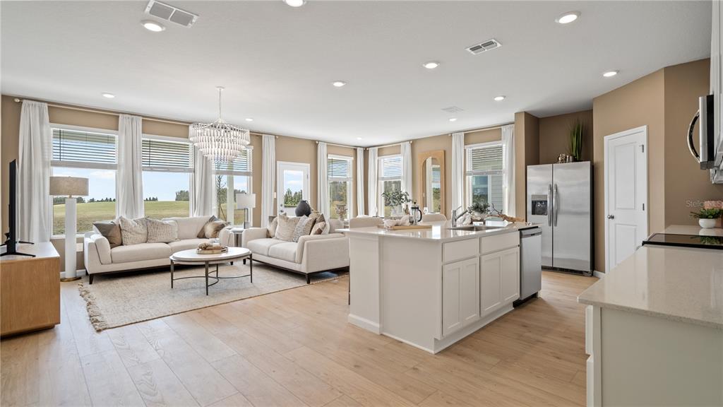 An open-concept living room and kitchen feature light wood floors, white cabinetry, and large windows — 3129 ROCKWOOD WAY, MINNEOLA, FL