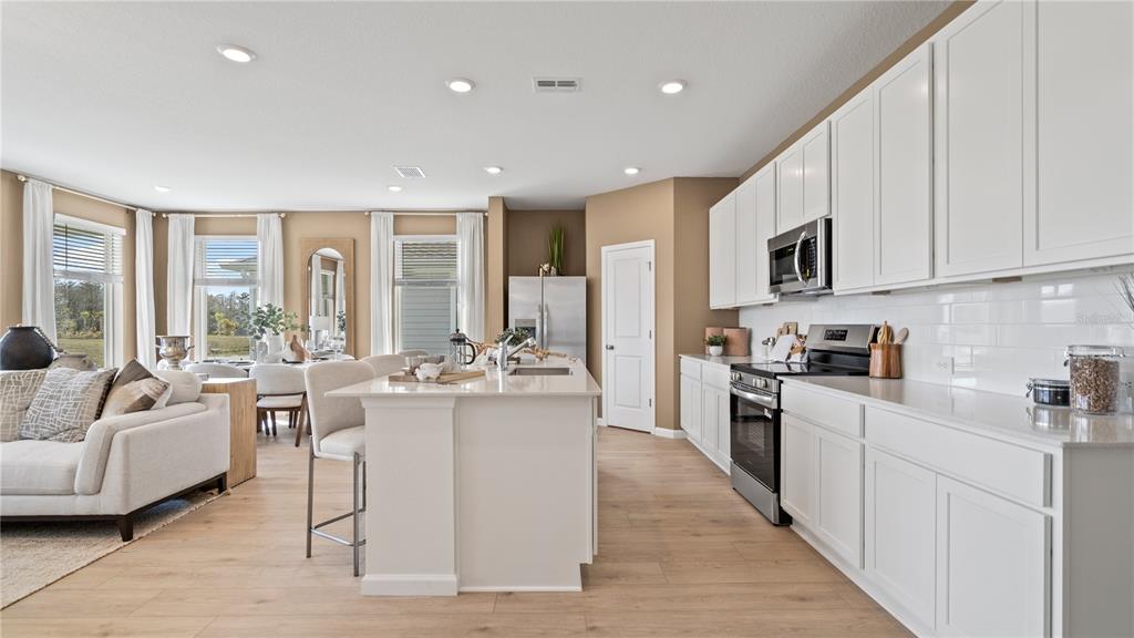 A modern kitchen with white cabinets and a central island opens into a living area — 3129 ROCKWOOD WAY, MINNEOLA, FL