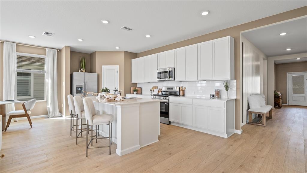 A modern kitchen features white cabinetry, a central island with bar seating, and light wood flooring — 3129 ROCKWOOD WAY, MINNEOLA, FL