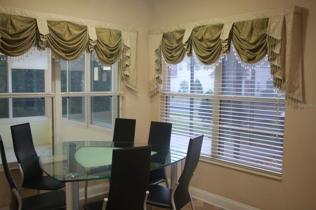 A dining area features a glass table, black chairs, and windows with ornate green valances — 6935 BRESCIA WAY, ORLANDO, FL