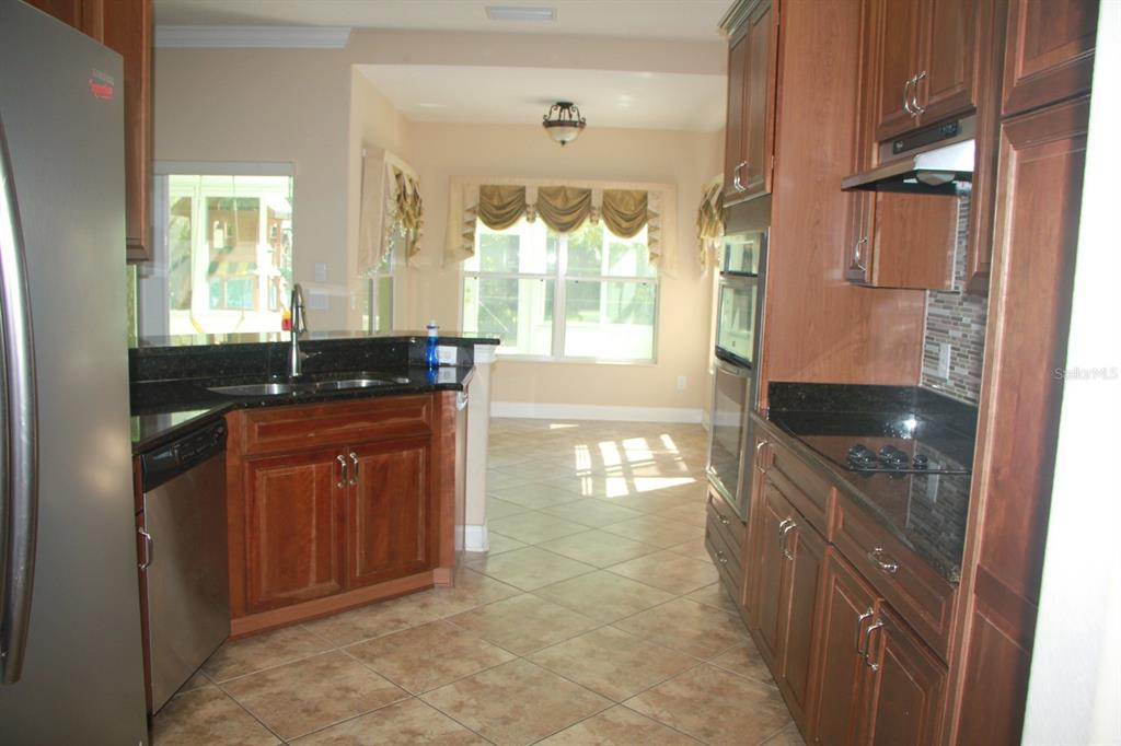 A kitchen with wood cabinets, dark granite countertops, stainless steel appliances, and tile flooring — 6935 BRESCIA WAY, ORLANDO, FL