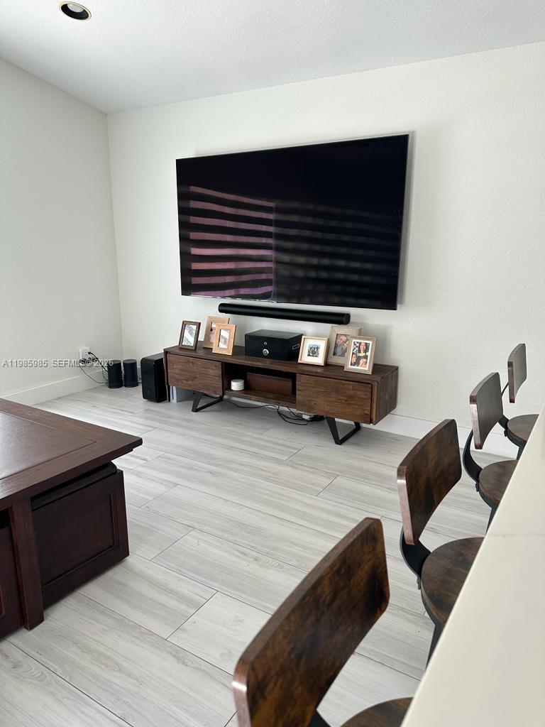 A living room features a wall-mounted television above a wooden media console and light flooring — 2484 SW 177th Ter, Miramar FL 33029, MIRAMAR, FL