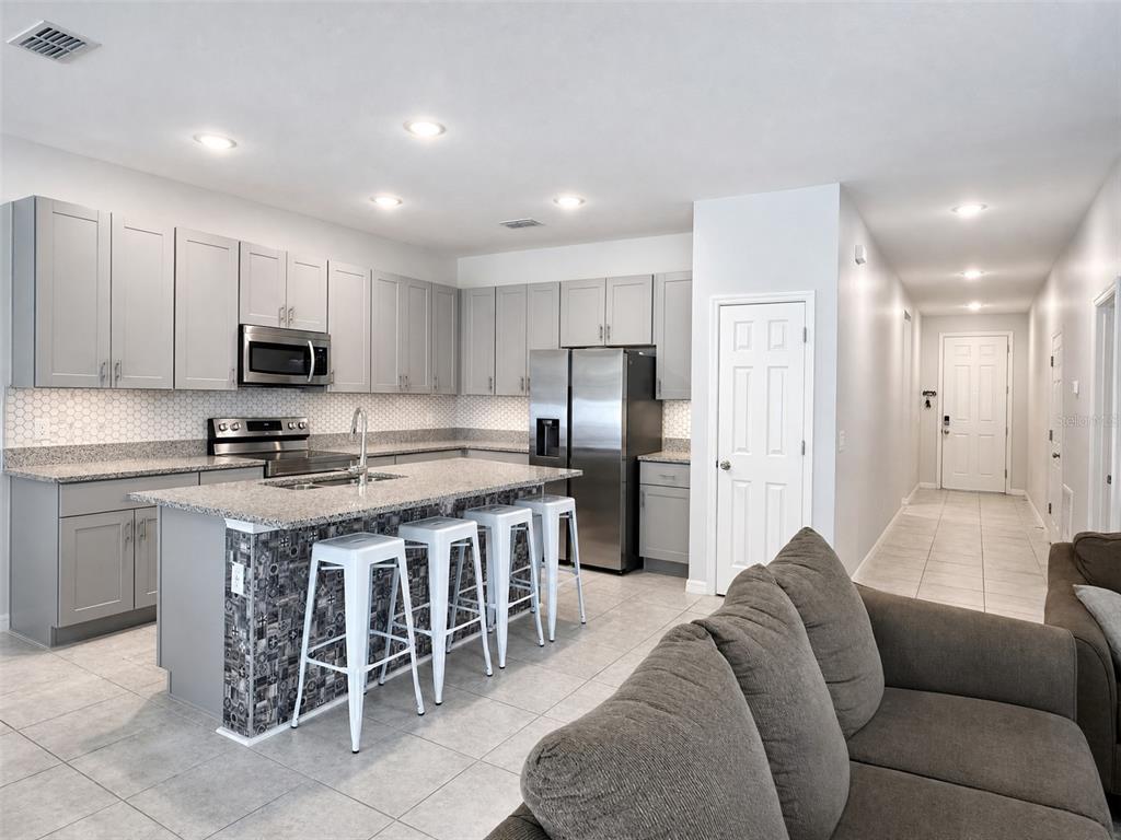 A kitchen with gray cabinets, granite countertops, a tiled island, and stainless steel appliances — 1622 WAY OF PEACE LANE, MASCOTTE, FL