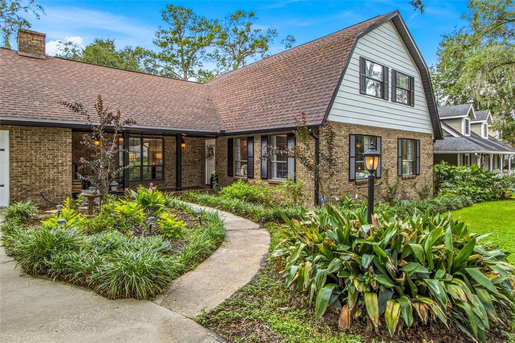 A brick house with a gambrel roof and a curved walkway through a landscaped garden — 527 COLONIAL DRIVE, BROOKSVILLE, FL